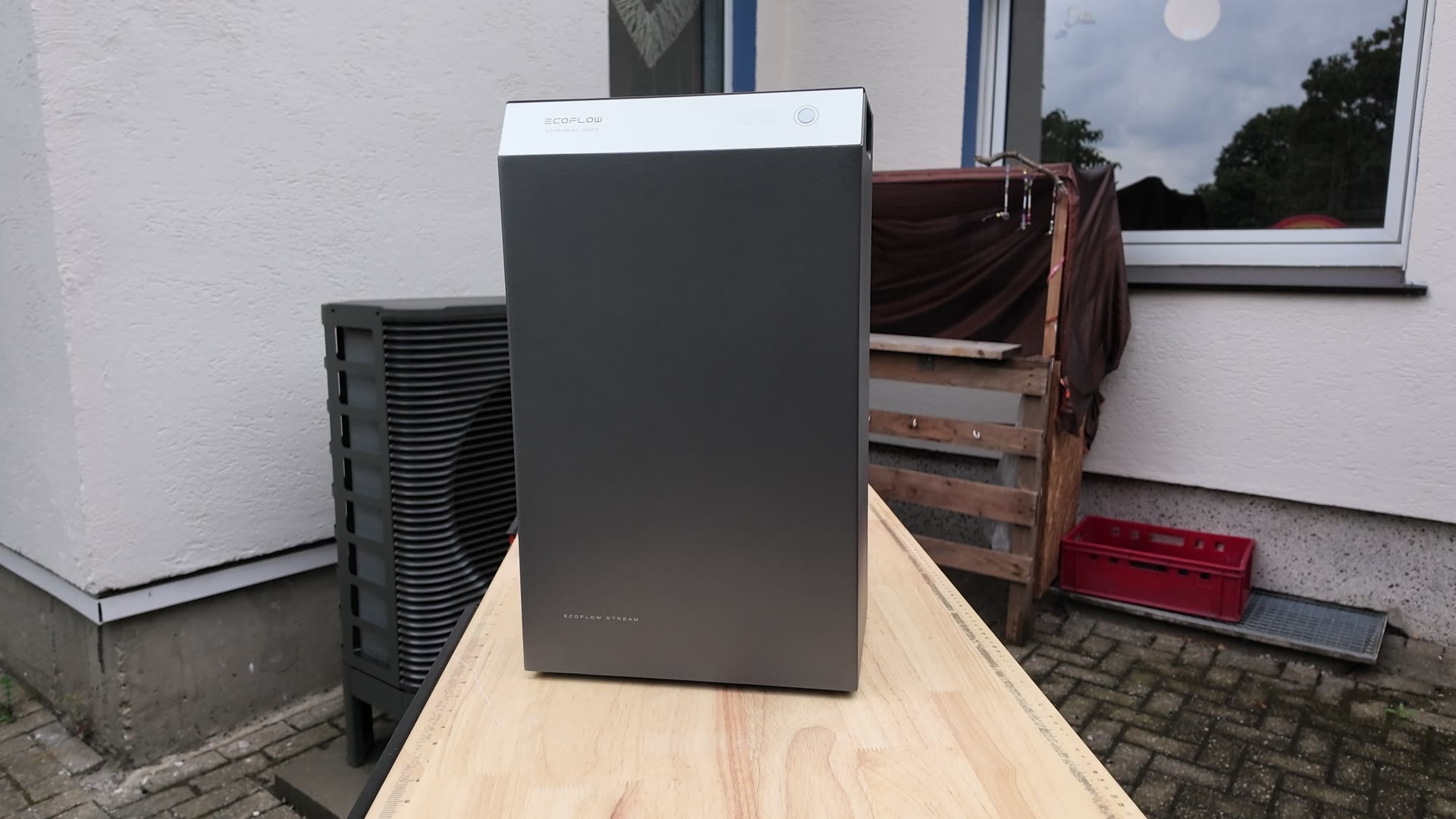 Der EcoFlow STREAM steht hochkant auf einer hellen Holzplatte vor einer Hauswand. Die Vorderseite ist dunkelgrau, oben sitzt ein heller Streifen mit EcoFlow-Schriftzug und Taster.