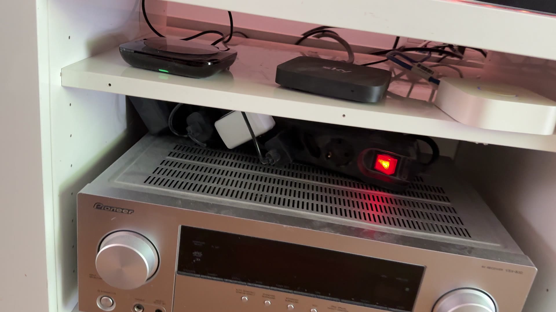 Regal mit einem silbernen Pioneer-AV-Receiver, darüber eine Sky-Box und weitere Geräte mit Kabeln