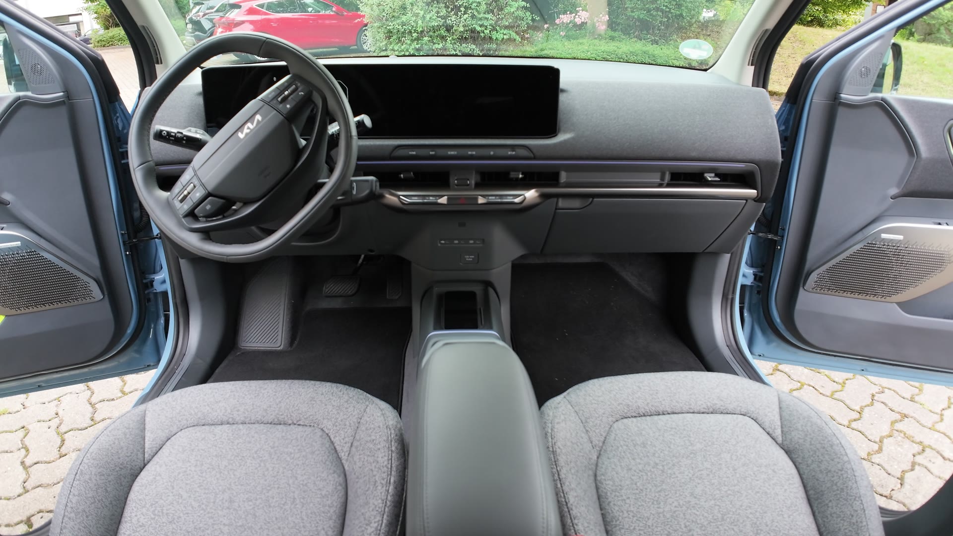 Blick von hinten auf das Cockpit des Kia EV2 mit Lenkrad, Bildschirm, Armaturenbrett und den beiden Vordersitzen, beide Türen sind geöffnet.